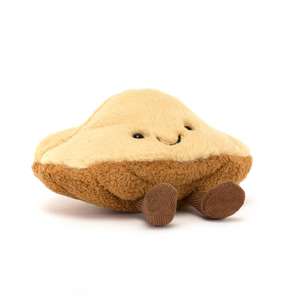 Jellycat brown madeleine shaped plush with a smiling face and brown feet on a white background. 