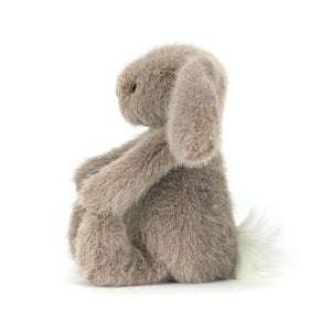Side view of a Jellycat fawn coloured bunny plush with a white fluffy tail on a white background.