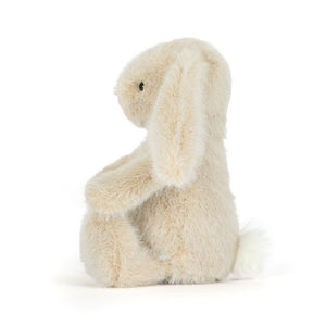 Side view of a Jellycat wheat coloured bunny plush with a white fluffy tail on a white background.