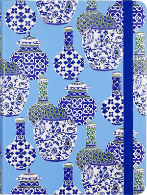 A midsize journal with a blue and white porcelain vases patterned cover and a blue elastic band.