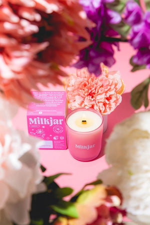 Pink Milkjar candle and packaging among colorful flowers on a pink background