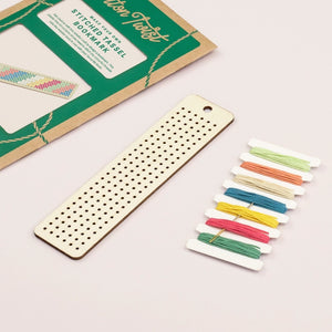 Wooden bookmark beside colourful threads and packaging on a light background. 