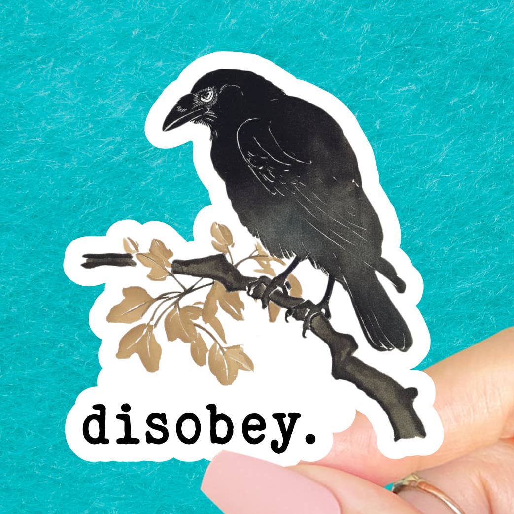 A sticker showing an image of a crow perched on a branc with leaves on a white background. The text 'disobey.' is printed under the crow. The sticker is held against a blue background. 