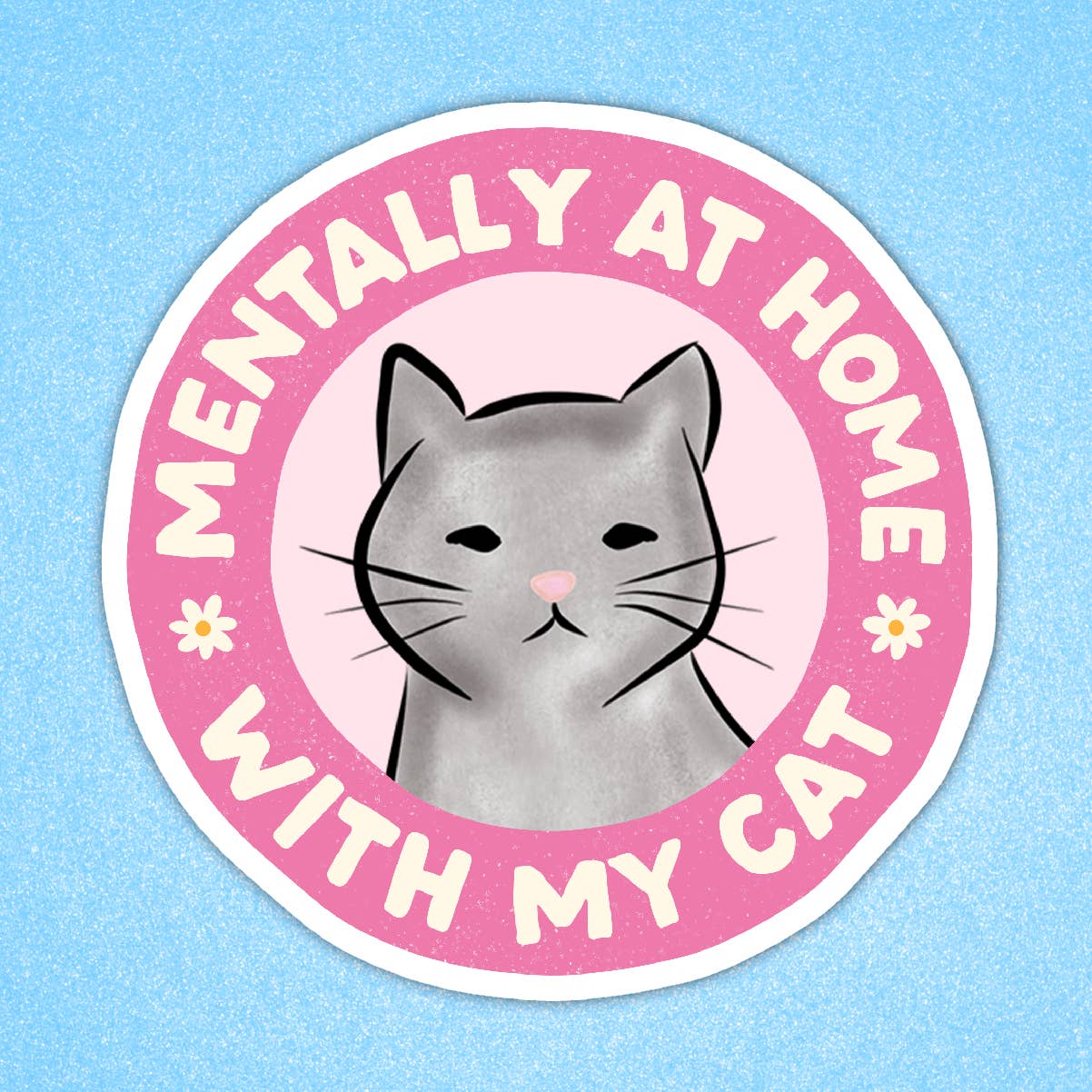 A round sticker with a pink border and white text reading 'Mentally at home with my cat', featuring an illustration of a grey cat face in the centre. Two white and yellow flowers sit beside the text in the border. 