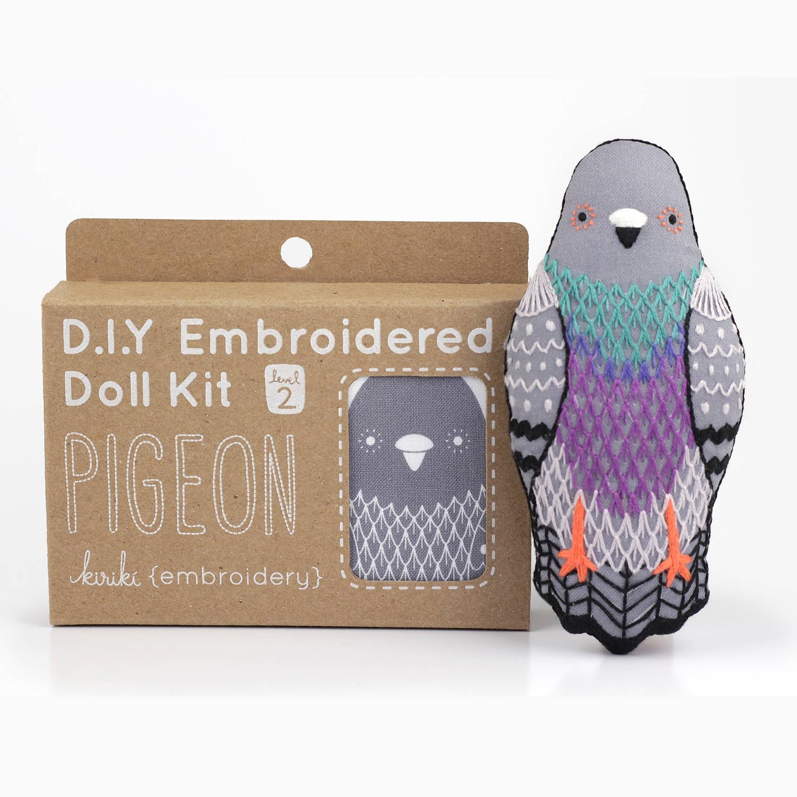A DIY embroidered doll kit box next to a finished embroidered pigeon doll plush on a white background. The box is brown with white text. 