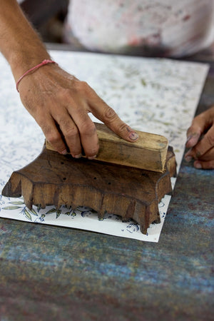 Hand using a wooden stamp to print a design on paper.