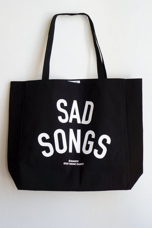 large black tote bag with white text that reads "sad songs"